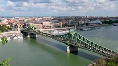 Budapest, Hungary, August 2022. Tilt footage of Liberty bridge with aerial view. Panorama of the city, large tourist boats moored along the bank of the Danube river.