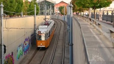 Budapest, Hungary, August 2022. Life in the city, in the background The Blna shopping center side by side people on the riverside danube. Vintage 2m tram descends underpass.