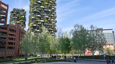 Milan, Lombardy, İtalya. Nisan 2023. Kütüphanedeki ağaçların bahçesindeki eğim görüntüleri, insanlar yürüyüş yolu boyunca yürür, dikey orman adı verilen iki kulenin altını çizer: düşük çevresel etki projesi