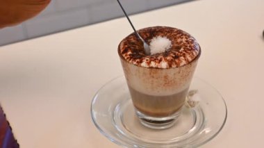 Kavramsal rahatlama görüntüsü: bir mocaccino 'nun köpüğünde şeker vardır, bir çay kaşığı beyaz bir kadının eli onu tüketme zevki için yavaş yavaş onu batırır..