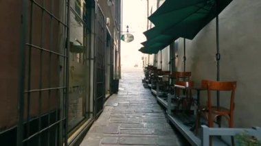 Cenova, Liguria, İtalya. 3 Haziran 2023. Tarihi merkezin ara sokaklarında yürürken, bir kafe masasının önünden geçiyoruz. Arka plandaki insanlar. Genoa Keşfediliyor.