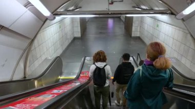 Prag, Çek Cumhuriyeti, 4 Ağustos 2023. Metrodaki yürüyen merdivenlerdeki görüntüler çalıştırılıyor. Önümüzde orta yaşlı bir kadın ve iki genç Kafkas. Uzun sarı saçlı bir kadın yanımızdan geçiyor..