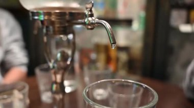Prag, Çek Cumhuriyeti, 4 Ağustos 2023. Absinthe 'in eski bir kasaba barına damlaya damlaya damlaya sallaya sürahide servis edilen büyüleyici yavaş çekim görüntüleri. Musluğa yakın çekim yap..