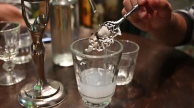 Prag, Çek Cumhuriyeti, 4 Ağustos 2023. Absinthe kaşığının üzerinde şeker küpü olan yavaş çekim görüntüsü: el onu anason içine daldırır ve karıştırır.