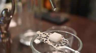 Prag, Çek Cumhuriyeti, 4 Ağustos 2023. Absinthe kaşığının üzerinde şeker küpü olan yavaş çekim görüntüleri: hazırlanma damlaları şekeri ıslatıyor.