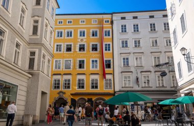 Salzburg, Avusturya, 15 Ağustos 2022. Mozart 'ın tarihi merkezdeki evinin fotoğrafı. Parlak sarı cephede Casa di Mozart yazılıdır. Sokaktaki insanlar, güzel bir yaz günü.