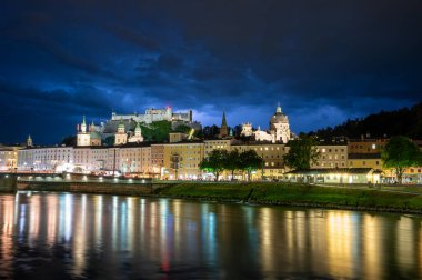 Salzburg, Avusturya, 15 Ağustos 2022. Nehre bakan tarihi merkezin büyüleyici gece çekimi. Arkada, tepede, kalede. Uzayı kopyala Dramatik gökyüzü, kalenin yakınındaki şimşek.