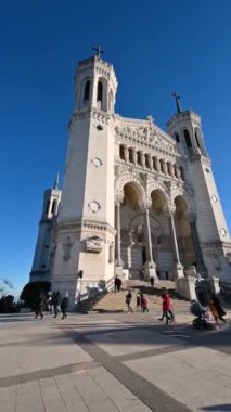 Lyon, Fransa, 27 Aralık 2023. Notre-Dame de Fourvire bazilikasının ön cephesinin dikey biçimi. Öğleden sonranın sıcacık ışığı yüzümüzü aydınlatıyor. İnsanlar kilise bahçesinde yürüyor..