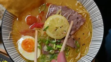 Bir tabak iştah açıcı ramen için güzel bir görüntü. Tahta çubuklar limon dilimini et diliminden haşlanmış yumurtaya taşır. Ortada sebze çorbası var..