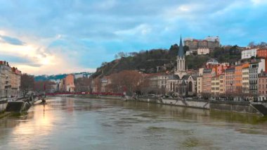 Lyon, Fransa, 27 Aralık 2023. Önünde kırmızı yaya köprüsü olan Aziz George Kilisesi 'nin yer aldığı ikonik nehir manzaralı bir görüntü. Güneş bulutların arasından bakıyor.