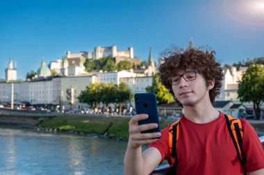 Salzburg, Avusturya, 15 Ağustos 2022. Genç beyaz bir adamın Padlock Köprüsü 'nden selfie çekmesi ve arka planda kalenin hüküm sürdüğü eski kasabanın....