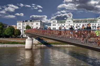 Salzburg, Avusturya, 15 Ağustos 2022. Bir sürü insan tarafından yürütülürken asma kilit köprüsünün güzel görüntüsü. Sayısız renkli asma kilit parmaklıklarda görülebilir. Güzel bir yaz günü.