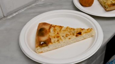 Pirinç keki üzerindeki yakın çekim görüntüleri: tipik Ligurian spesiyali, restoranlarda ve Liguria, İtalya 'da sokak yemeği olarak satılıyor. Bir el alır ve dilimi kaldırır. Yakındaki bir plakada diğer özellikler.