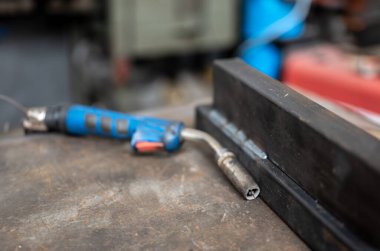 Kaynak tabancasına yakın plan, iki kaynaklı metal çubuğun yanında. Çalışmanın kavramsal görüntüsü, metal işçiliği, işçilik. Boşluğu kopyala.