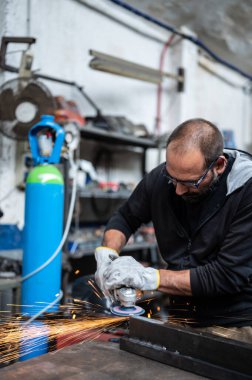 Metal çubuktaki esnek disk öğütücüsünü kullanarak: Araç yüzeye değdiğinde, sayısız turuncu kıvılcım yansıtılır. Dikey format. Atölyede metal işleme kavramı, el işi.