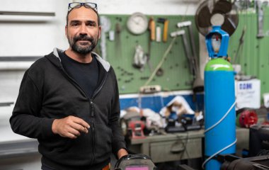 Kaynak seansında bir demircinin portresi. Bir sigara içme fırsatını değerlendirir, kaynakçının kaskı sağ altta görülebilir. Atölye ile bulanık arkaplan.