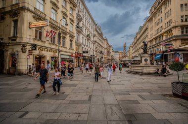 Viyana, Avusturya, 18 Ağustos 2022. Alışveriş caddelerinden birinin manzarası: moda markaları görülebilir, cadde insanlarla dolu. Arka planda, Veba Sütunun altın tepesi görülebilir.