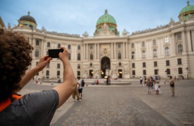 Viyana, Avusturya, 18 Ağustos 2022. Ausgrabungen Michaelerplatz 'da genç beyaz bir turist cep telefonuyla hatıra fotoğrafı çekiyor. Arka plandaki insanlar. Teknoloji kullanılarak tatilde yaşam tarzı.