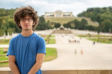 Viyana, Avusturya, 20 Ağustos 2022. Kıvırcık saçlı ve gözlüklü genç bir adamın güzel portresi. Arkasında Schonbrunn Sarayı 'nın büyüleyici manzarası var..