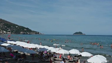 Alassio, İtalya, 14 Temmuz 2024. İkonik yavaş çekim sahnesi, deniz önü ile. Sudaki ya da beyaz şemsiyelerin altındaki insanlar. İtalyan denizinde tatil ve rahatlama kavramı.