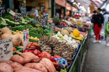 Viyana, Avusturya, 23 Ağustos 2022. Naschmarkt pazarında, mevsimlik sebzelerle yakın çekim. Patates, arpacık soğanı, sarımsak, yeşil fasulye, enginar. İnsanlarla olan bulanık arkaplan.
