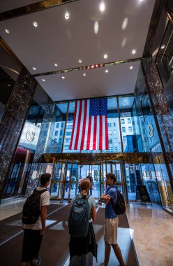 New York, New York, ABD. 14 Ağustos 2024. Trump Tower 'ın lobisindeki insanlar. İnsanlar gökdelenin içini ziyaret etmeye giderler. Büyük bir Amerikan bayrağı belirgindir. Dikey biçim.