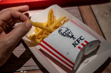 Viyana, Avusturya, 23 Ağustos 2022 KFC patates kızartması ve sandviç paketinin yakın çekimi. El sandviçi tutuyor, cipsler logoyla birlikte karton kutuda. Sektördeki büyük şirketlerde fast food.