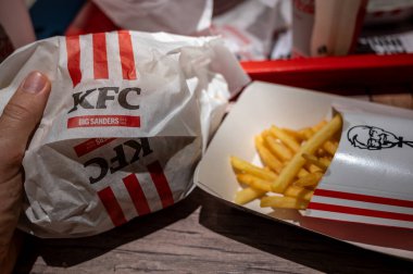 Viyana, Avusturya, 23 Ağustos 2022 KFC patates kızartması ve sandviç paketinin yakın çekimi. El sandviçi tutuyor, cipsler logoyla birlikte karton kutuda. Sektördeki büyük şirketlerde fast food.