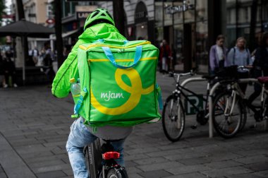 Vienna, Austria, August 23, 2022. Shot in a street in the historic center, a worker of the rider company mjam. He is on his bicycle to make a delivery. Selective focus. clipart