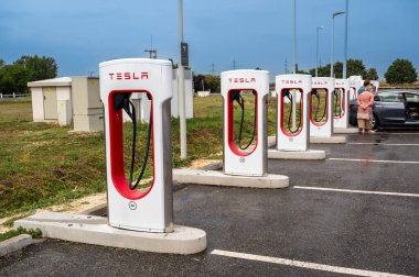 Budapeşte, Macaristan otoyolu. 24 Ağustos 2022. Tesla bir dinlenme alanında hızlı şarj istasyonları. Arka planda bir araba yakıt ikmali yapıyor. Sahipleri arabanın yanında..