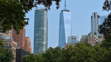 New York, ABD, 16 Ağustos 2024. Battery Park 'tan One World Trade Center' a doğru çekilen görüntüler. Finansal bölgenin modern gökdelenlerini çevreleyen ağaçlar. Eğik hareket.