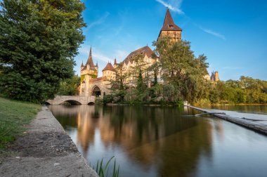 Budapeşte, Macaristan. 27 Ağustos 2022. Geniş açılı mercek, Vajdahunyad Kalesi 'ne doğru alçak açı. Uzun pozlama. Sıcak öğleden sonra ışığı ön tarafı aydınlatıyor. Peri masalı atmosferi, seyahat yerleri.