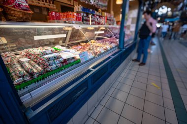 Budapeşte, Macaristan. 29 Ağustos 2022. Kapalı market, bir et satıcısının tezgahının ayrıntıları. Çeşitli kesikler tip ve fiyat etiketi ile gösterilir. Bir müşteri mallara bakıyor..