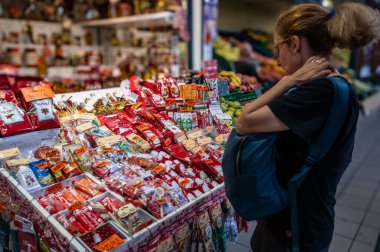 Budapeşte, Macaristan. 29 Ağustos 2022. Kapalı piyasa, bir baharat satıcısının tezgahının detayları. Ambar renkli paketlerle dolu. Orta yaşlı bir kadın mala bakıyor..