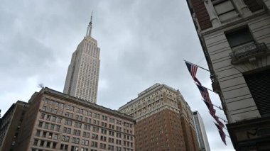 New York City, ABD, 19 Ağustos 2024. Şehrin ikonik bir görüntüsü: Empire State Binası karanlık akşam gökyüzüne karşı duruyor. Sağda, Amerikan bayrakları esintide hareket ediyor. Seyahat yerleri.