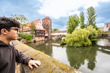 Nuremberg, Almanya, 1 Ağustos 2023. Genç beyaz bir adam, nehrin büyüleyici manzarasına hayran kalıyor. Yarı ahşap ev suya yansıyor. Nuremberg 'i keşfetmek ve keşfetmek.