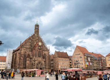 Nuremberg, Almanya, 1 Ağustos 2023. Yağmurlu bir günde görkemli pazar meydanı. İnsanlar meyve, sebze ve sokak yiyeceklerinin oradan geçiyor. Gökyüzündeki kara bulutların geçişi.