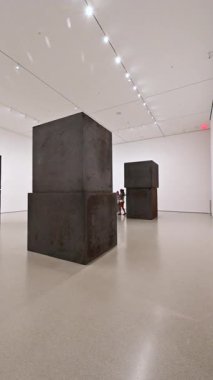 New York City, ABD, 20 Ağustos 2024. MoMA, Modern Sanatlar Müzesi. Beyaz bir odanın içinde büyük koyu renk blokları olan yeni bir sergi. Ziyaretçiler odadan geçer. Dikey biçim.
