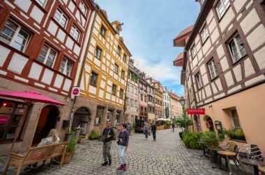 Nuremberg, Almanya, 1 Ağustos 2023. Tanner 'ların sokağı: Eski şehrin tüm cazibesine sahip renkli ve yarı keresteli evlerin cephelerine sahip. İnsanlar taş kaplı cadde boyunca yürür.