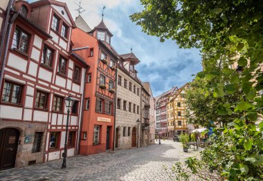 Nuremberg, Almanya, 1 Ağustos 2023. Tanner 'ların sokağı: Eski şehrin tüm cazibesine sahip renkli ve yarı keresteli evlerin cephelerine sahip. İnsanlar taş kaplı cadde boyunca yürür.