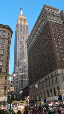 New York City, ABD, 20 Ağustos 2024. Şehir simgesinin dikey görüntüleri: Empire State Binası şehir manzarasında göze çarpar. Mavi saat. İnsanlar gelip gidiyor, sarı taksiler geçiyor. Seyahat yerleri