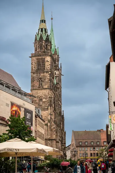 Nuremberg, Almanya, 2 Ağustos 2023. Yağmurlu bir günde, St. Lorenz Kilisesi 'nin dörtte üçü görünüyor. Sokaktaki insanlar şemsiye kullanıyor. Dikey olarak görüntülendi.