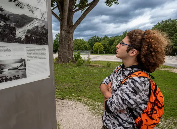 Nuremberg, Almanya, 3 Ağustos 2023. Kıvırcık saçlı ve gözlüklü beyaz bir adam Nazi parti alanındaki bilgi işaretlerine bakıyor..