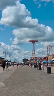 New York City, ABD, 21 Ağustos 2024. Coney Adası sahil şeridi boyunca yapılan yürüyüşün dikey görüntüsü, arka plandaki lunapark gezintisi. İnsanların yanından geçiyoruz. Güzel bir yaz günü.