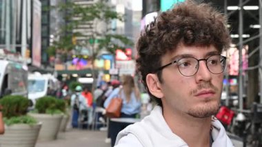 New York City, ABD, 21 Ağustos 2024. Şehir hayatı: kıvırcık saçlı ve gözlüklü beyaz bir adam Broadway 'in bulanık arka planında selfie çekiyor. Teknoloji kullanarak yaşam tarzı.
