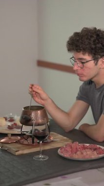 Kıvırcık saçlı ve gözlüklü beyaz bir adamın dikey görüntüleri. Bir masada oturmuş, sığır burginyon yiyor ve şarap içiyor. Lezzetli yemeklerden zevk alma tarzı..