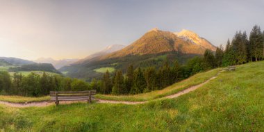 Berchtesgaden Ulusal Parkı, Yukarı Bavyera Alpleri, Almanya, Avrupa 'da gün batımında Hintersee Gölü yakınlarında yol ve bank ile Meadow. Gökyüzü yolu kırpılıyor