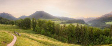 Berchtesgaden Ulusal Parkı, Yukarı Bavyera Alpleri, Almanya, Avrupa 'da gün batımında Hintersee Gölü yakınlarında yol ve bank ile Meadow. Gökyüzü yolu kırpılıyor