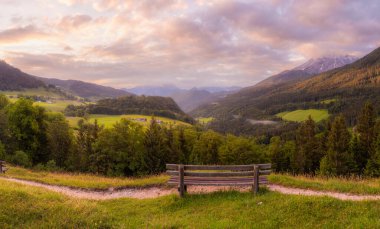 Berchtesgaden Ulusal Parkı, Yukarı Bavyera Alpleri, Almanya, Avrupa 'da gün batımında Hintersee Gölü yakınlarında yol ve bank ile Meadow. Gökyüzü yolu kırpılıyor