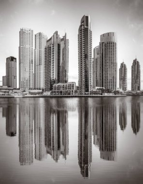 Tek renkli şehir gökdelenleri bulutlu bir gökyüzü altında sakin suyu yansıtan gökdelenler, kentsel gelişim konsepti, Dubai Marina Körfezi BAE